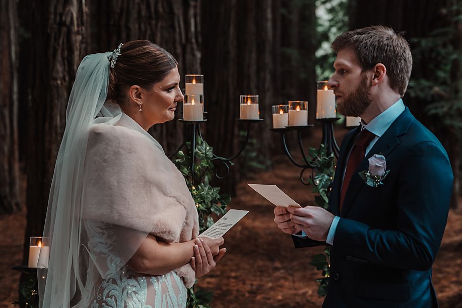 Couple exchanging vows in a forest setting surrounded by candlelight and tall trees during an intimate ceremony.