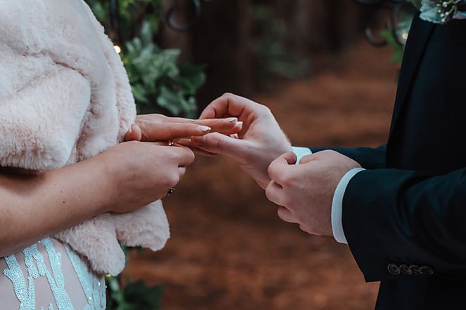 Close-up of hands exchanging wedding rings during romantic outdoor ceremony.