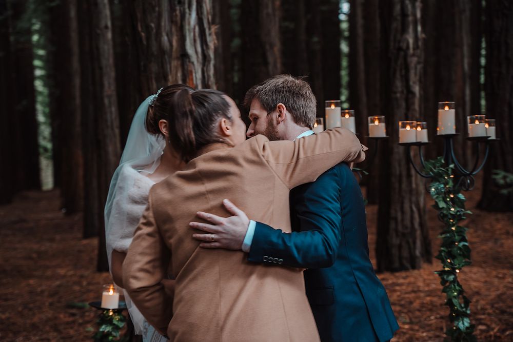 A couple embraces surrounded by candlelit lanterns in a romantic forest setting at dusk.