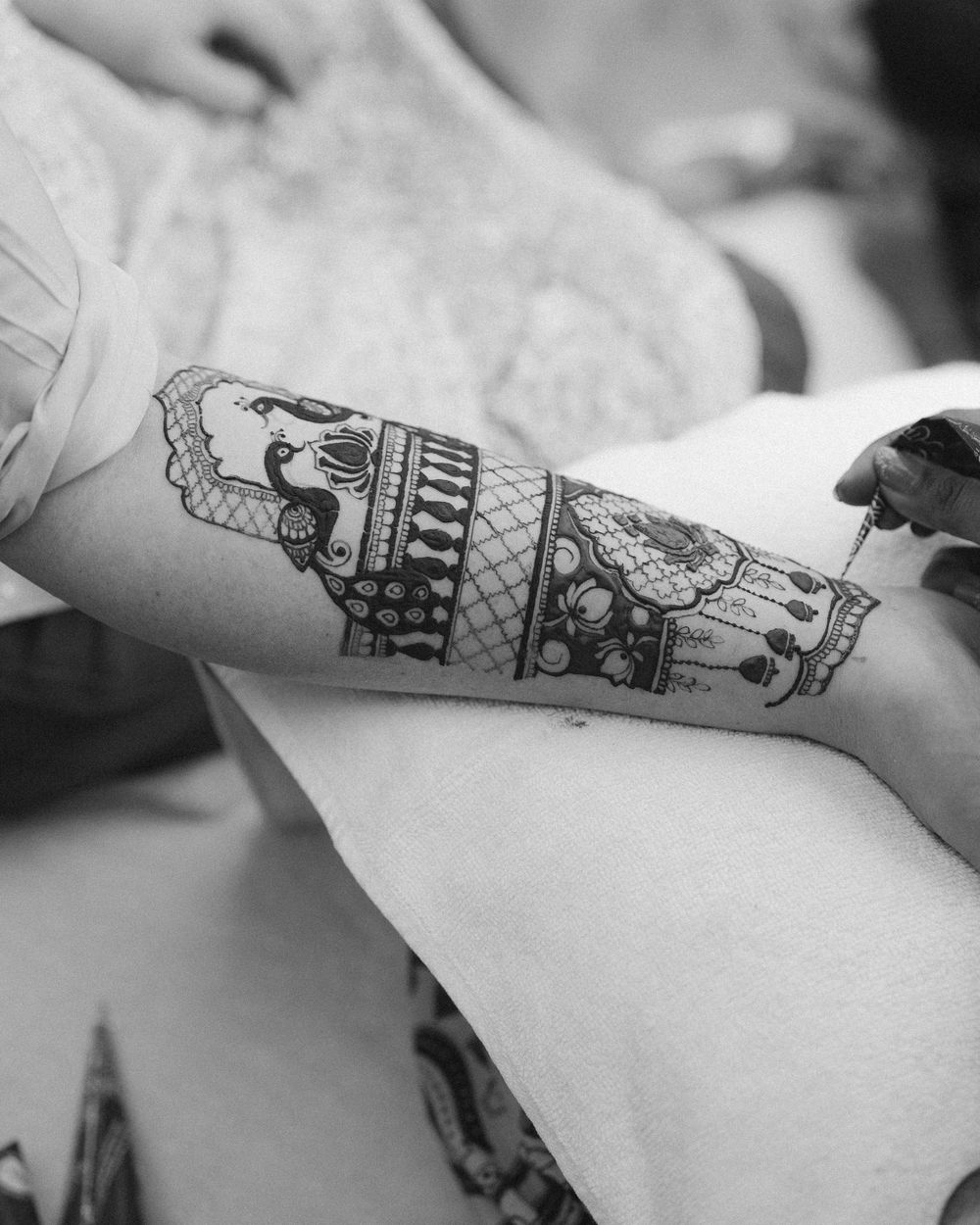 Black and white close-up of intricate henna designs on an arm.