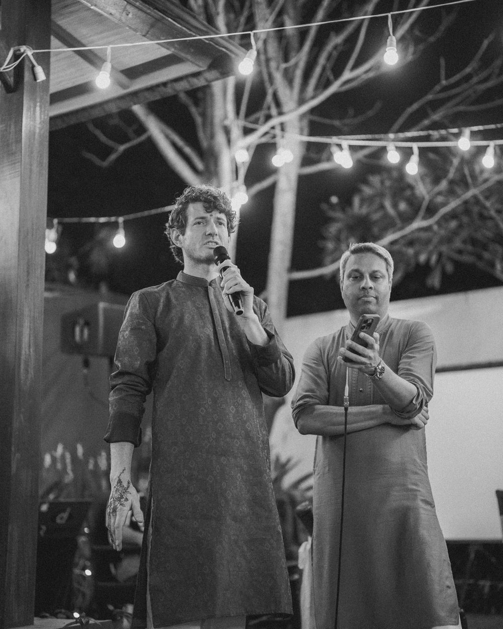 People performing karaoke under string lights at an outdoor venue.