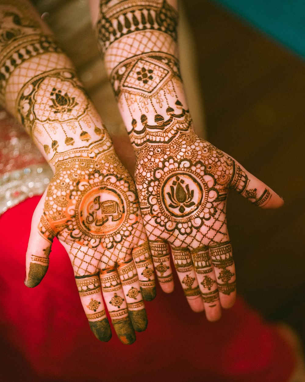 Detailed henna designs on palms displayed against red fabric background.