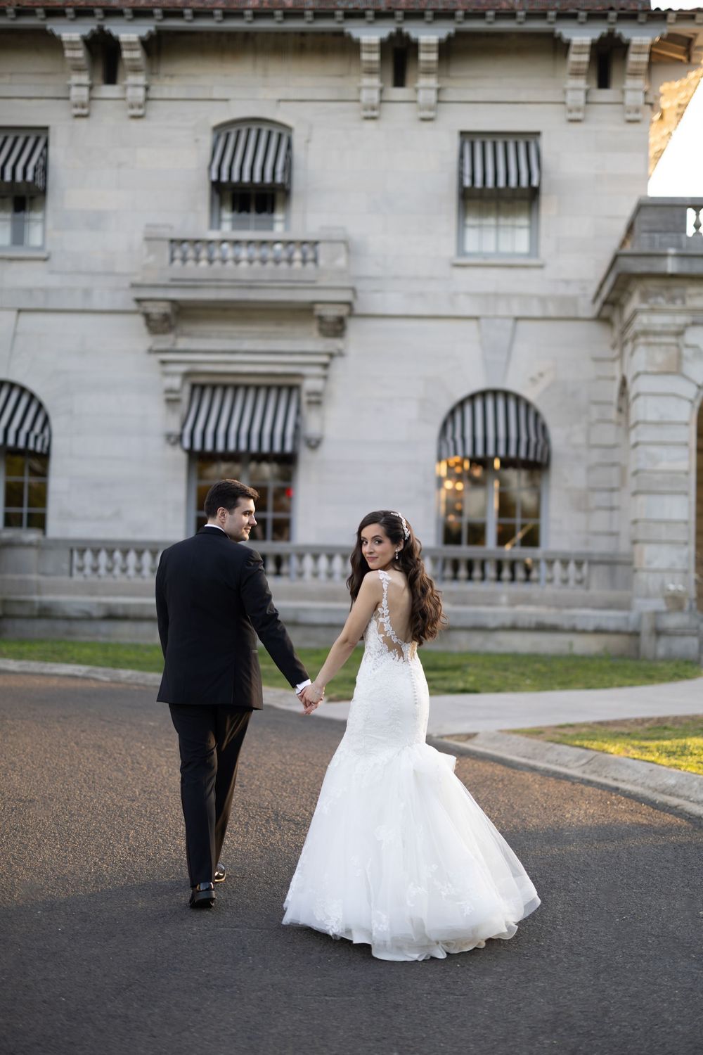 Young couple in formal wear dancing and spinning across a grand building's driveway in a romantic moment.