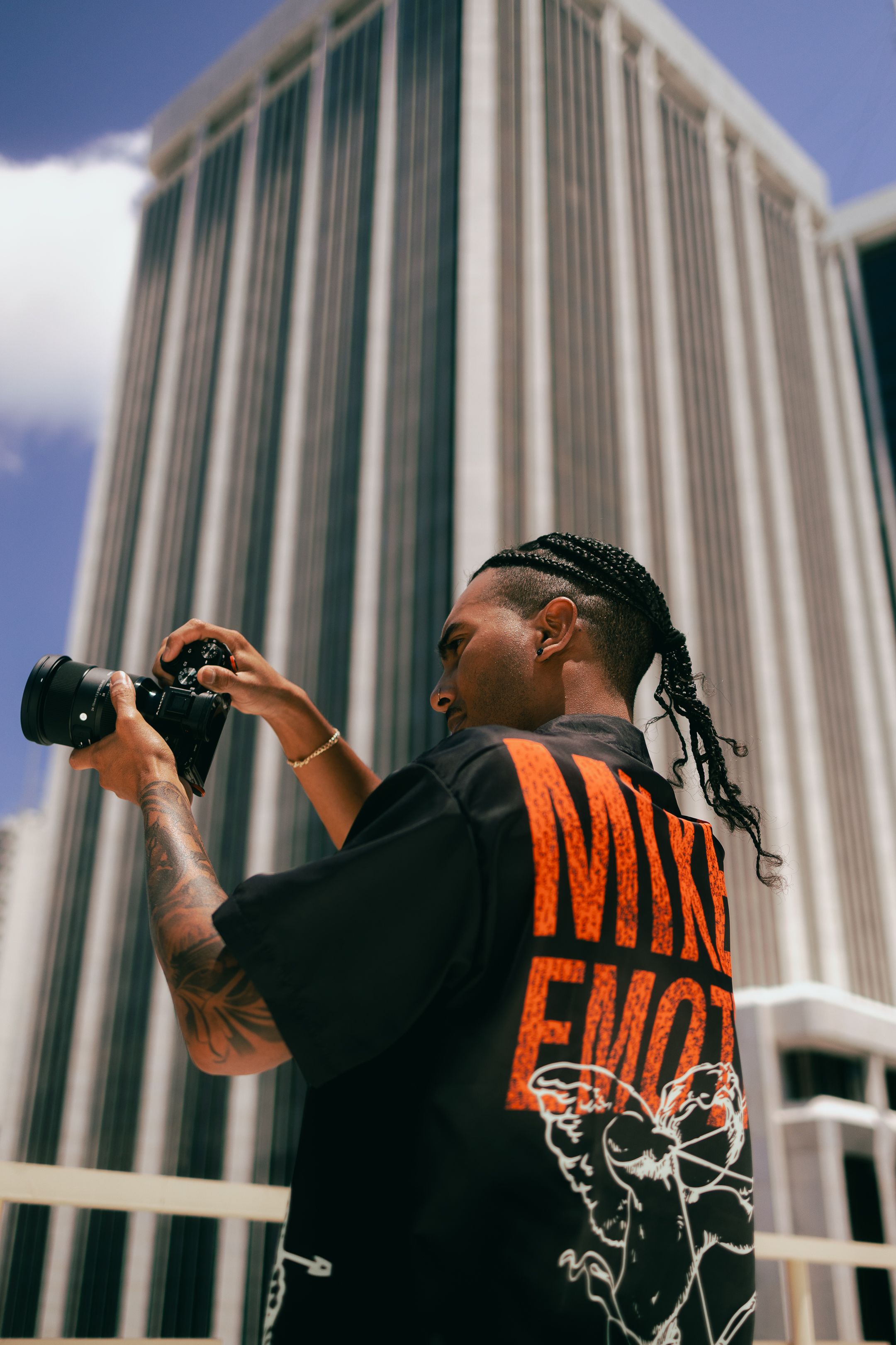 Model in red graphic tee leaning near Miami skyscraper, Zara-inspired urban streetwear fashion editorial shot for Pinterest + Instagram
