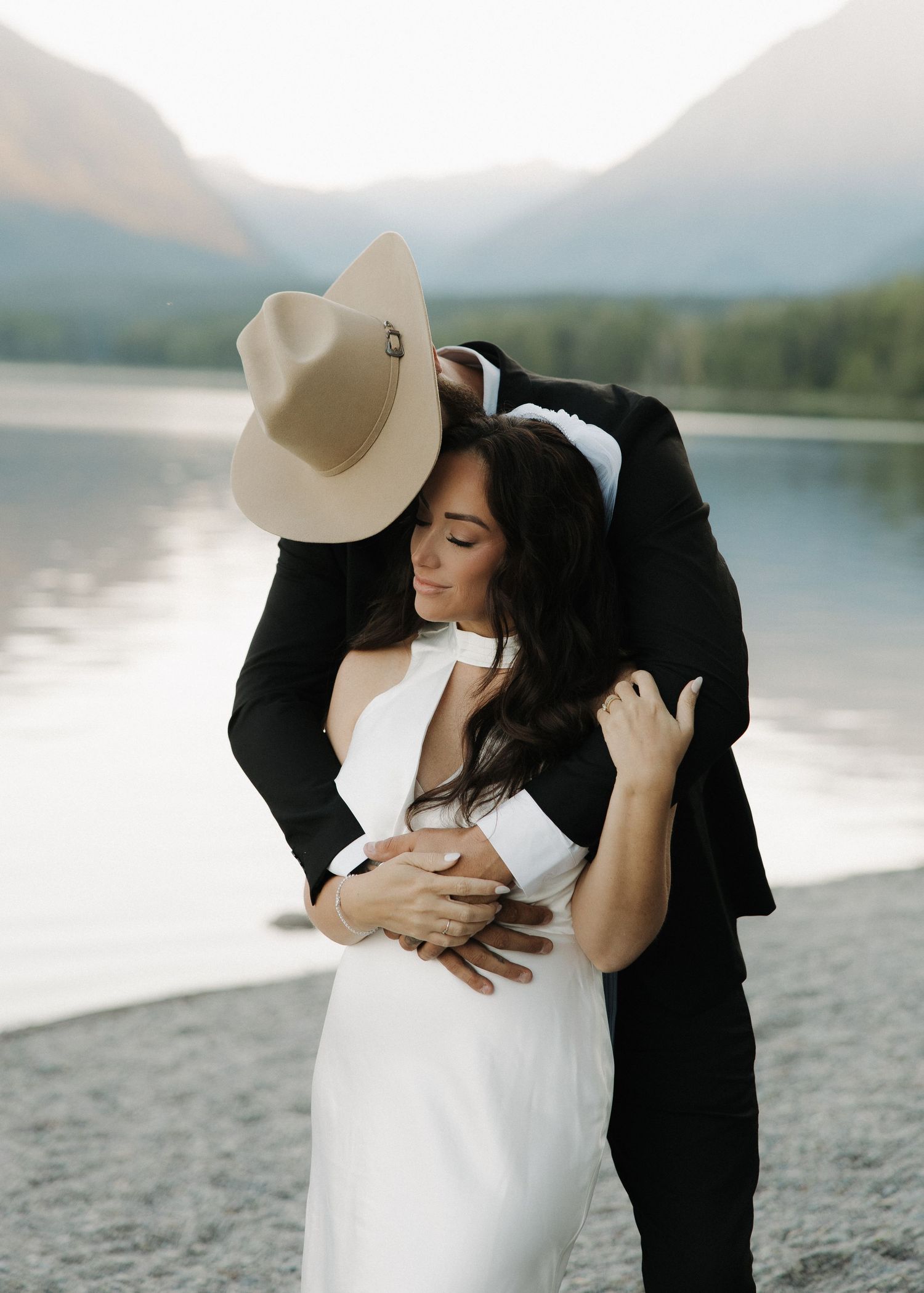 A romantic lakeside moment between a couple in contrasting black and white attire near misty mountains.