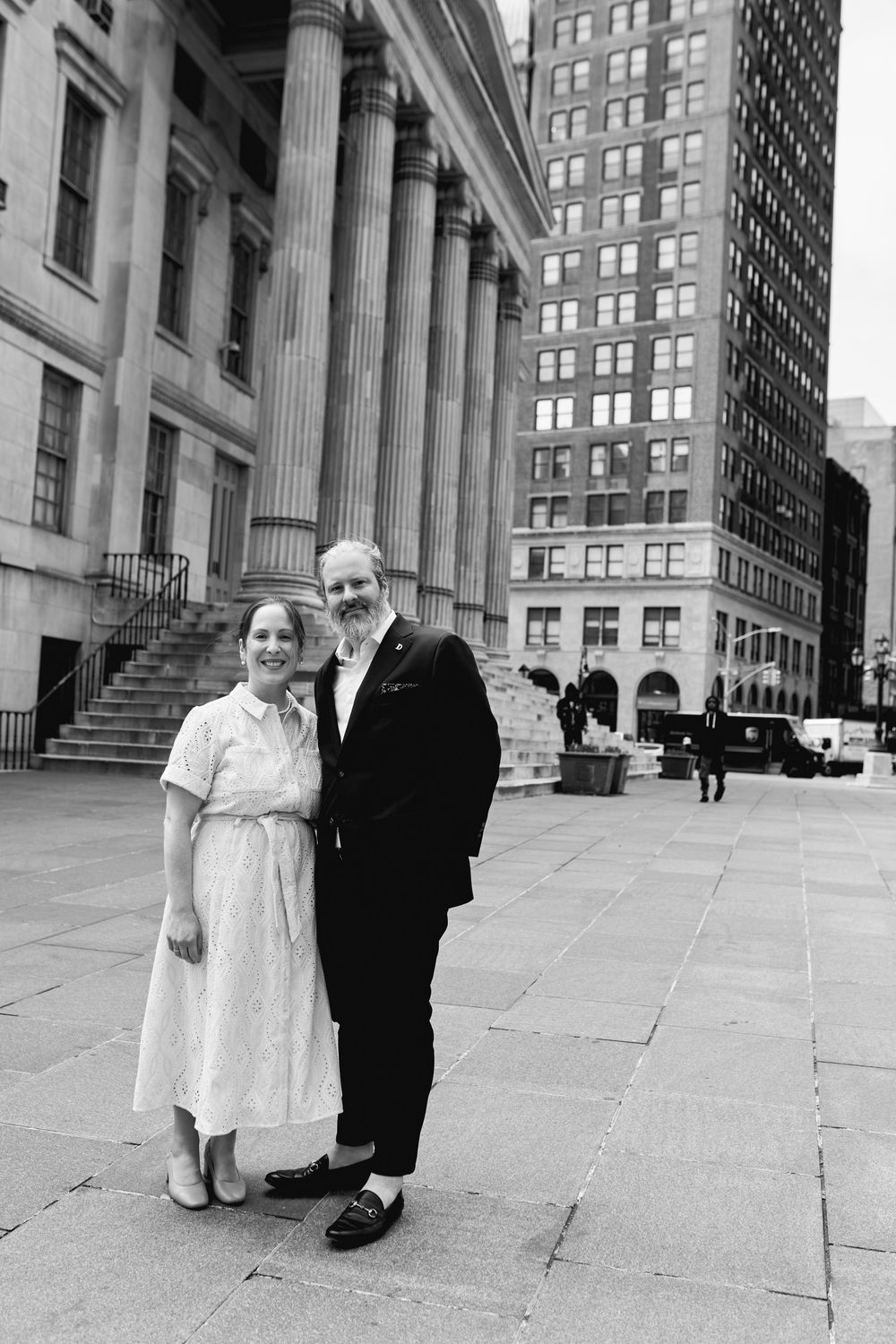 Black and white photo series of a couple standing on stone steps of a classic architectural building in an urban setting. Wedding photograph