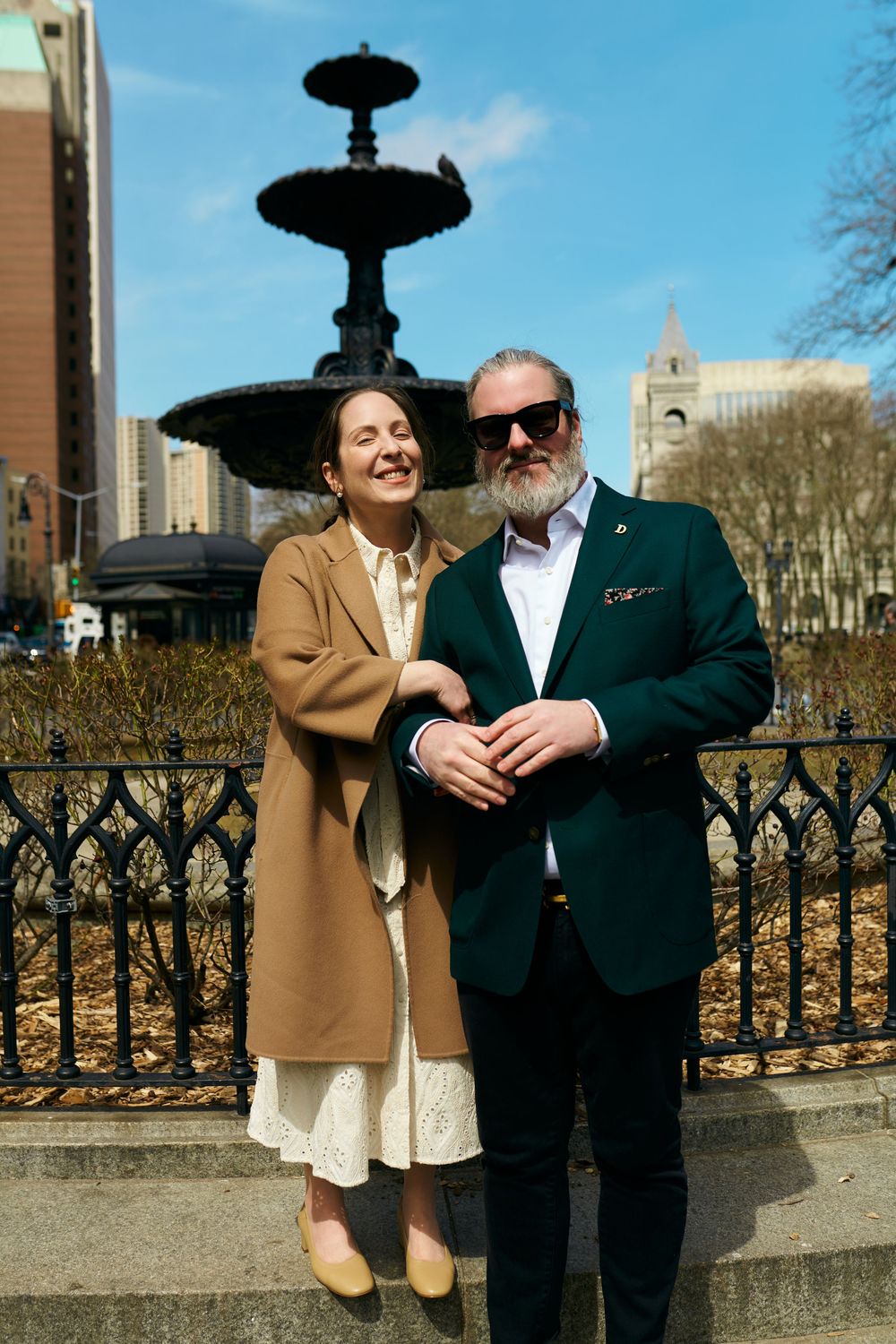 Couple in casual attire sharing a sweet moment while sitting on stone steps outdoors on a sunny day. Wedding photography