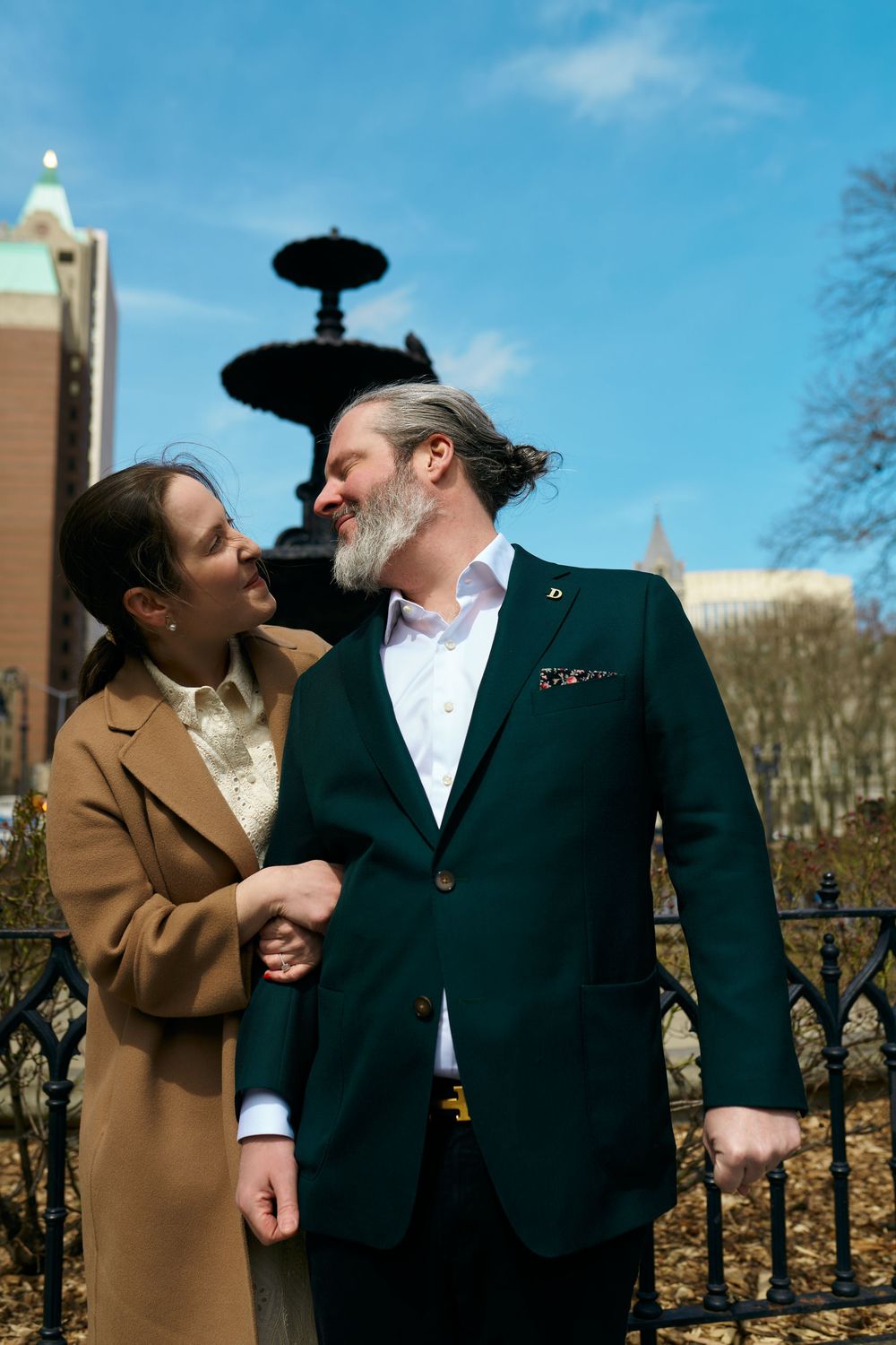 Couple in winter attire sharing a romantic moment on an iron railing balcony against a bright blue sky. Wedding photography