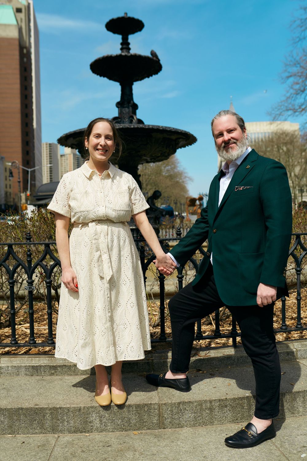 Two people pose together by an ornate black fountain in an outdoor urban setting. Wedding photography