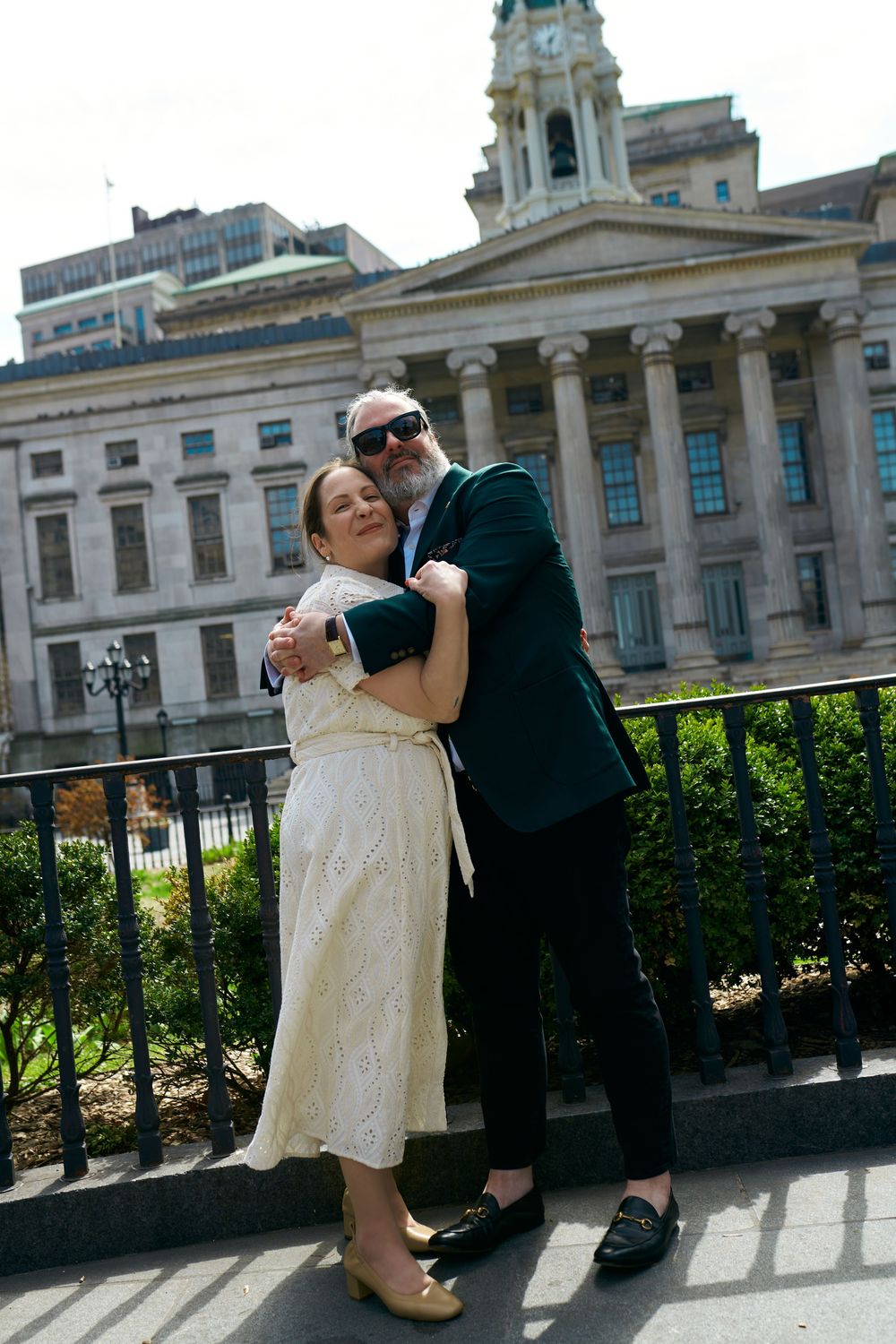 A couple shares a romantic moment in front of a grand neoclassical building with columns and a clock tower. Wedding photography