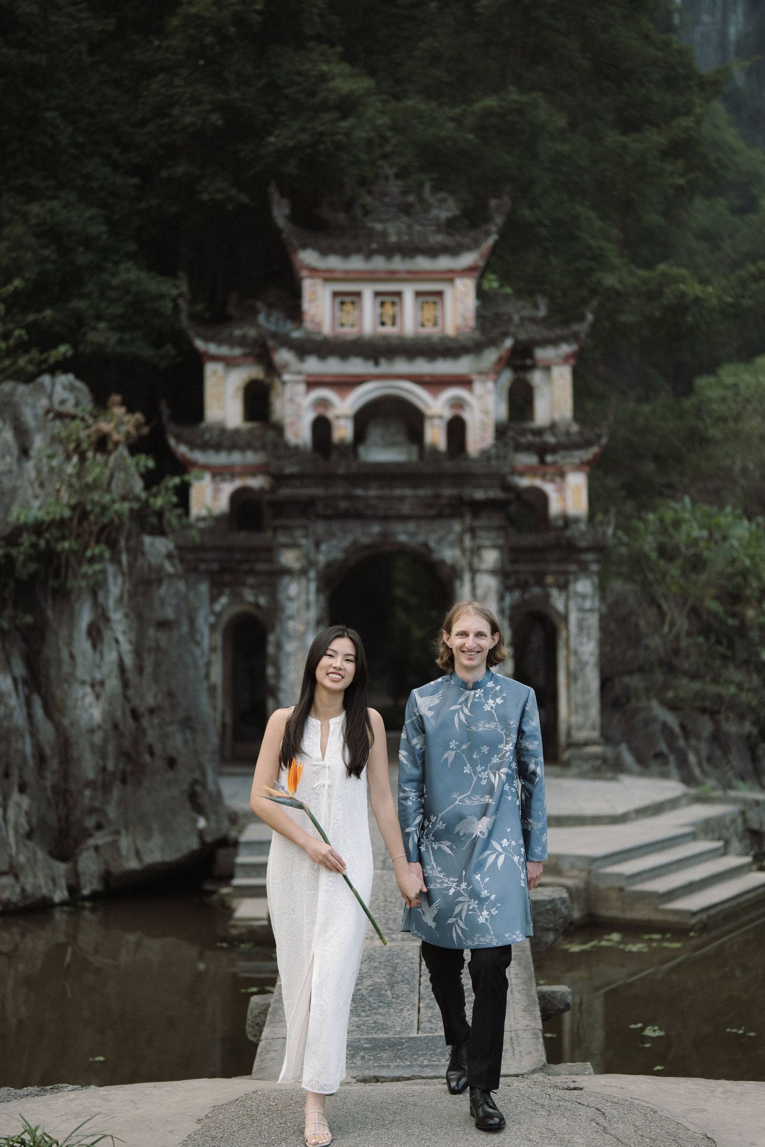 Couple taking romantic photos near traditional Asian architecture and stone walls.