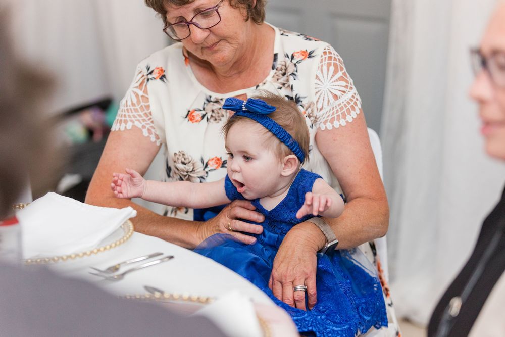A baby in a bright blue outfit is shown being held while glancing at a book during a reading session.