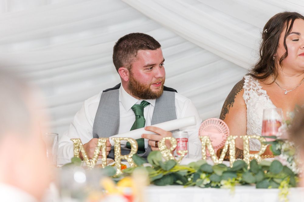 A panoramic view of wedding guests seated at a reception table decorated with greenery garlands and candlelight.