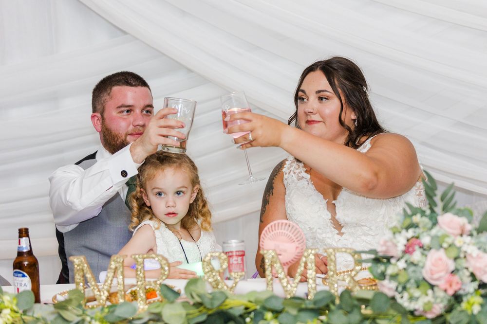 Wedding party members raise their glasses in a toast at the head table decorated with floral centerpieces.