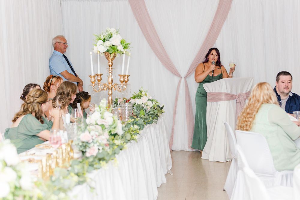 Wedding reception features elegant table settings with white floral centerpieces and soft pink drapery in the background.