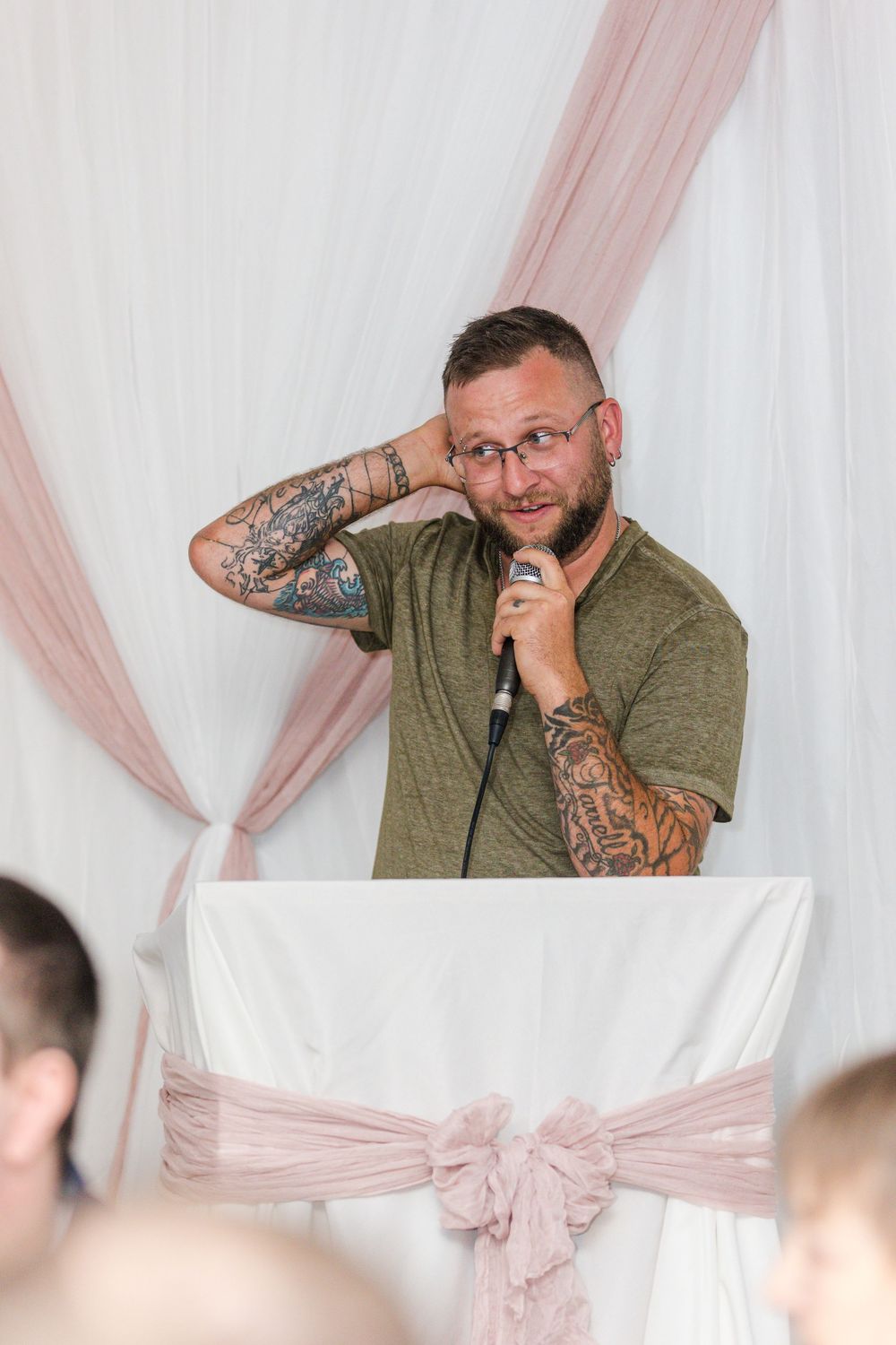 A candid emotional reaction captured during what appears to be a wedding reception against a pink and white backdrop.