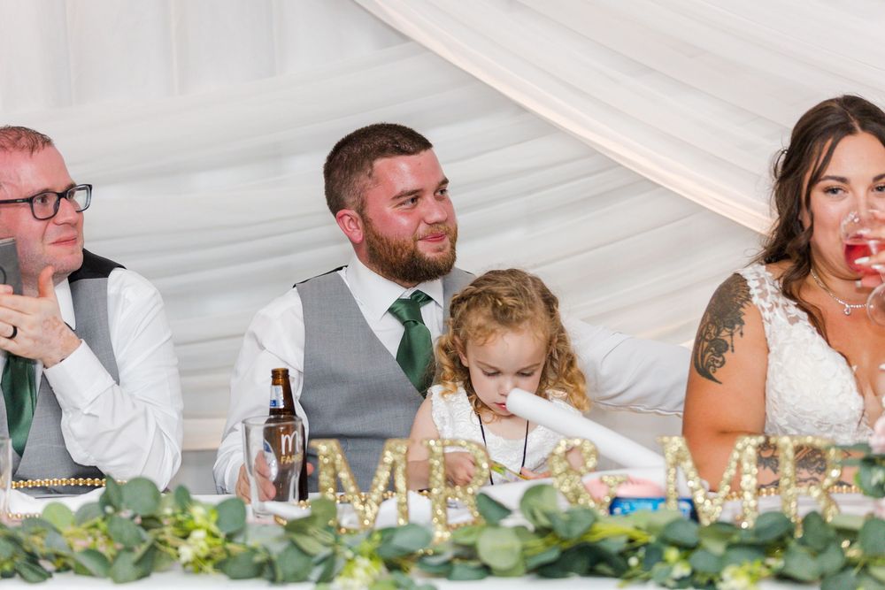 Wedding guests sharing laughter and candid moments at a reception table decorated with greenery garland.