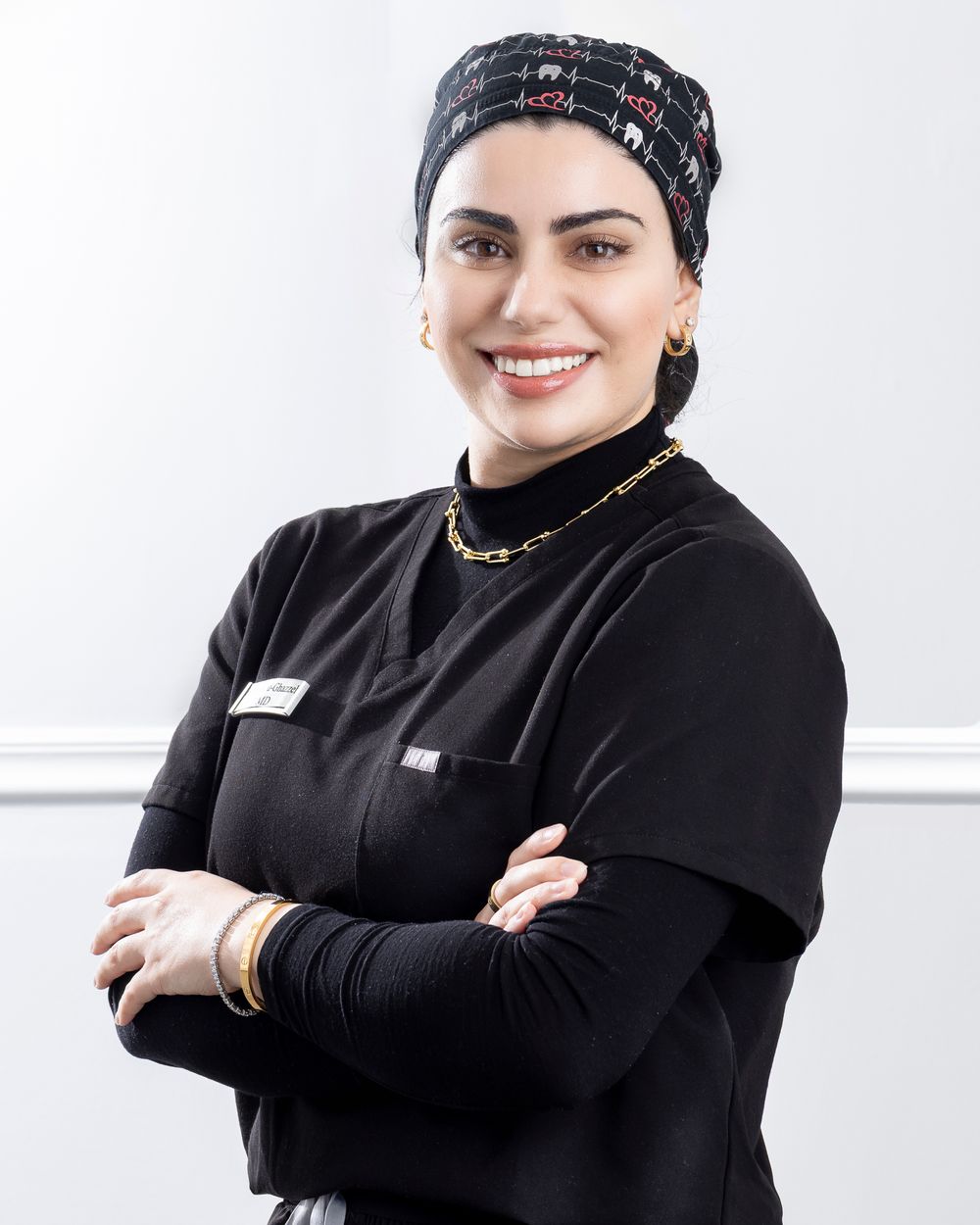 Healthcare worker in black scrubs and patterned cap poses professionally against light background.