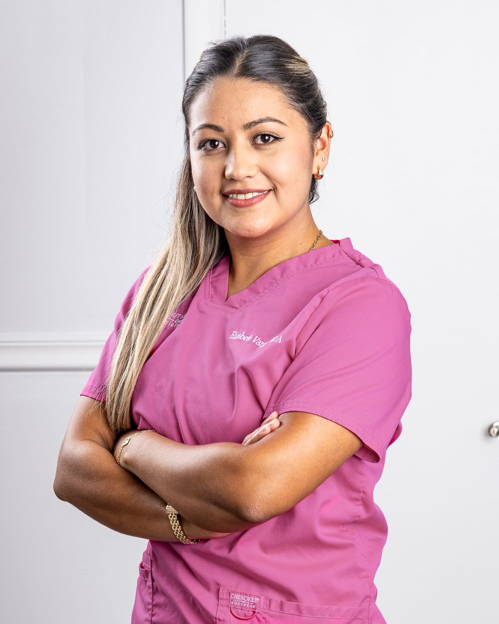 Healthcare professional in pink scrubs poses confidently against white background.