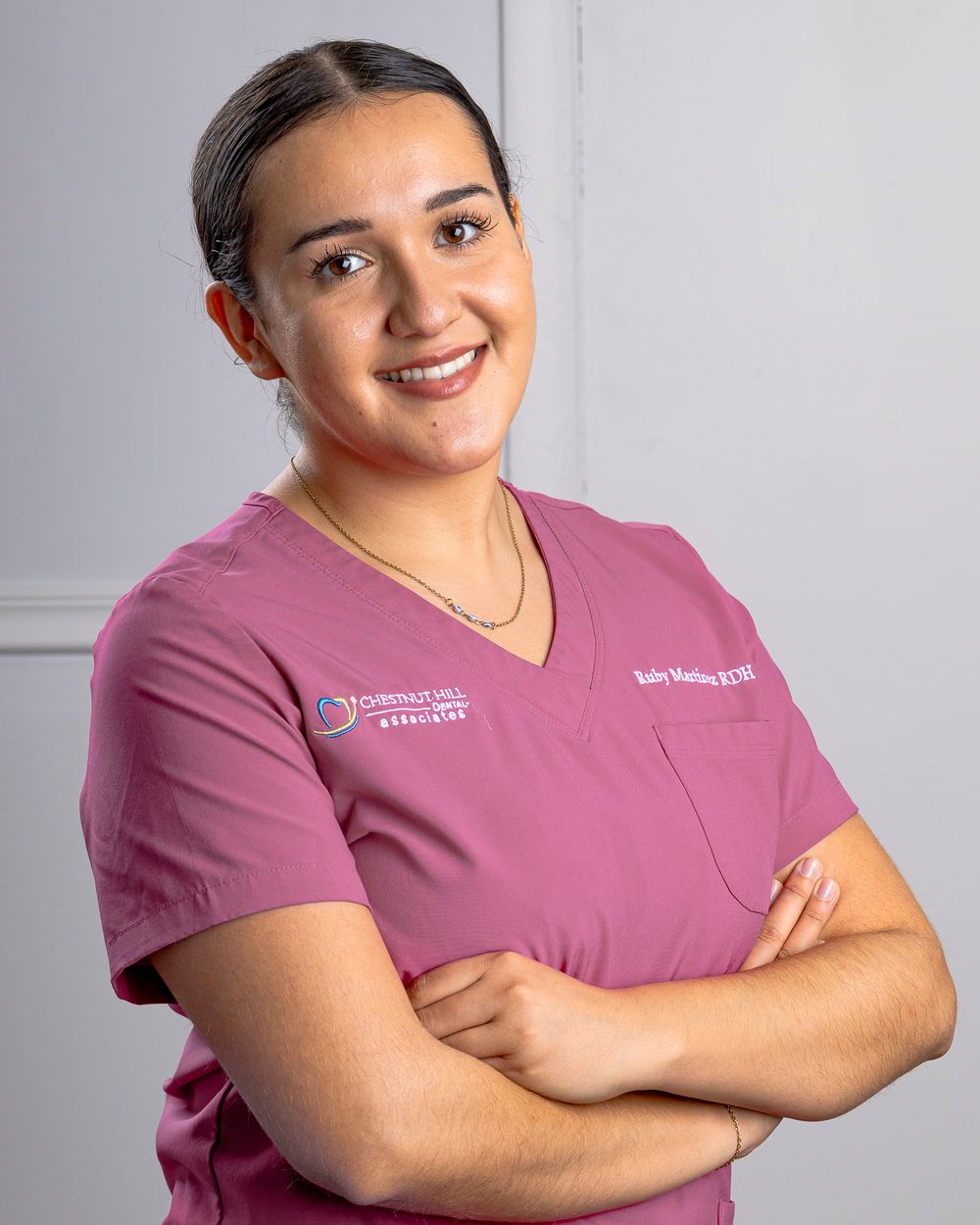 Medical staff member in mauve scrubs smiles warmly in studio setting.