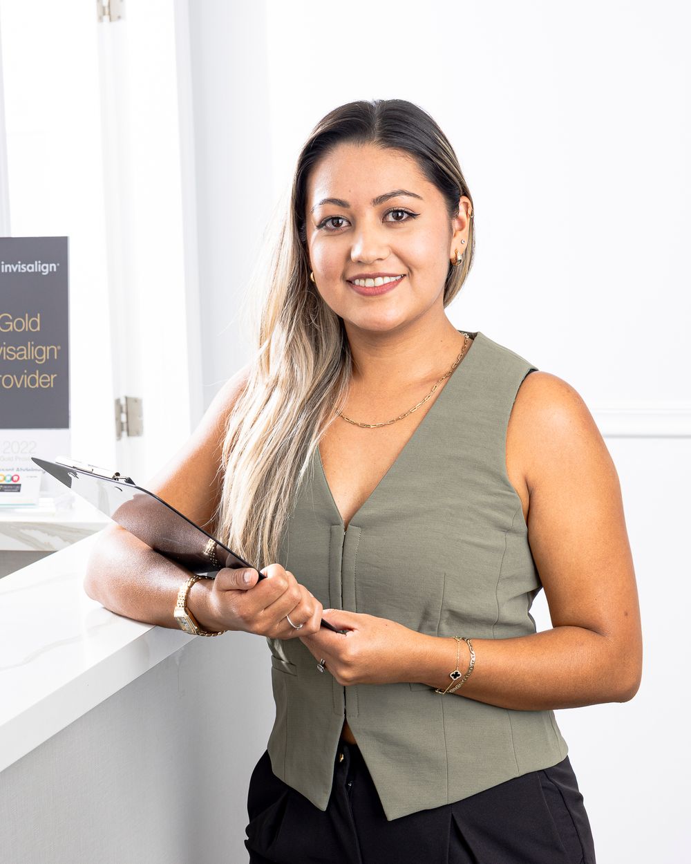 Professional wearing olive green vest poses in modern office environment.