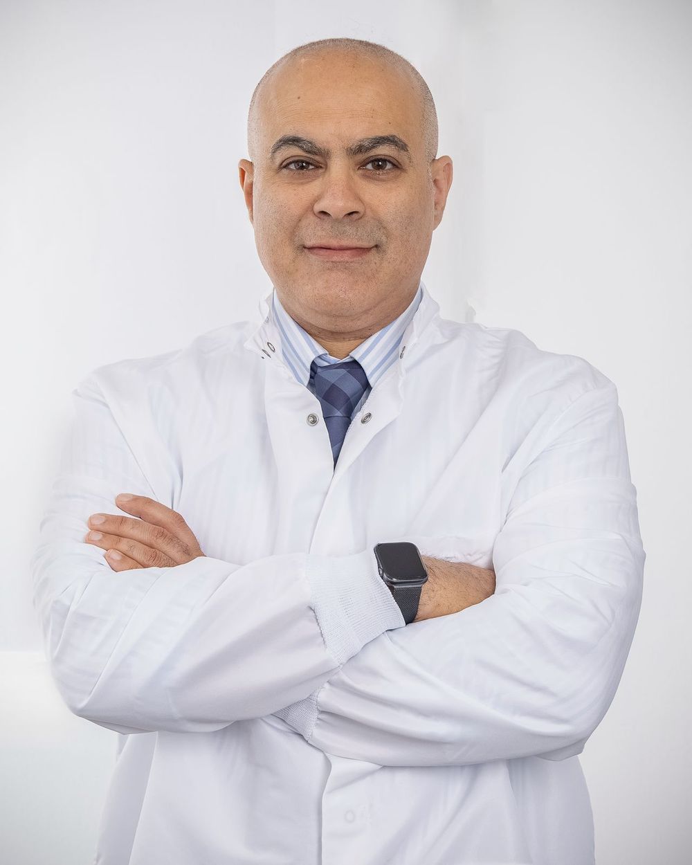 Medical professional in white coat stands confidently with arms crossed.