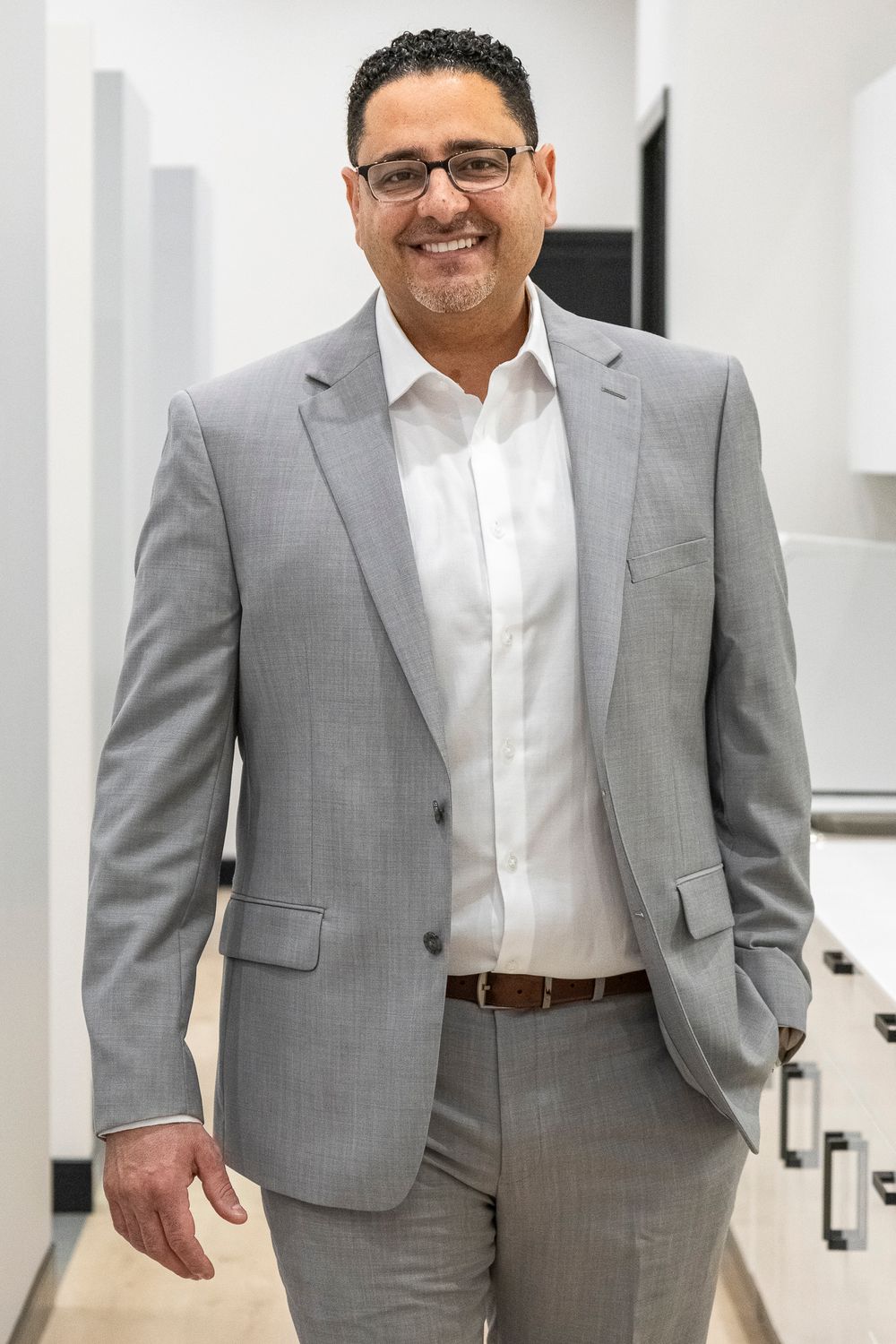 Professional in grey suit smiling in modern office hallway.