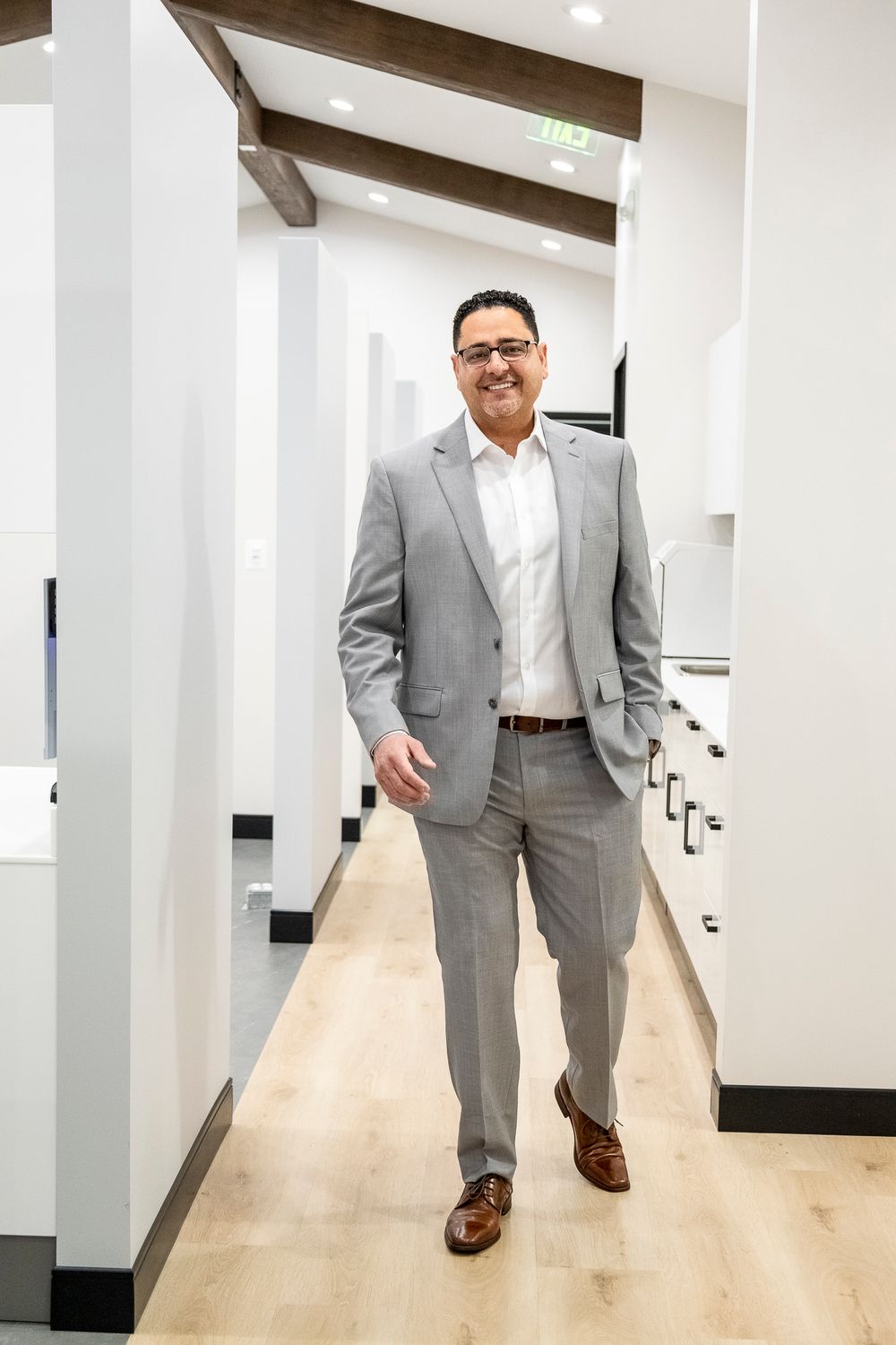 Professional wearing a light gray suit walks confidently down a modern hallway with wooden floors.