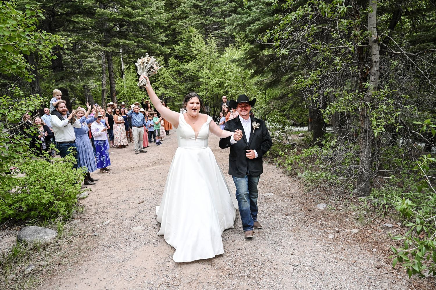 Wedding party walking along a forested mountain trail in formal attire.