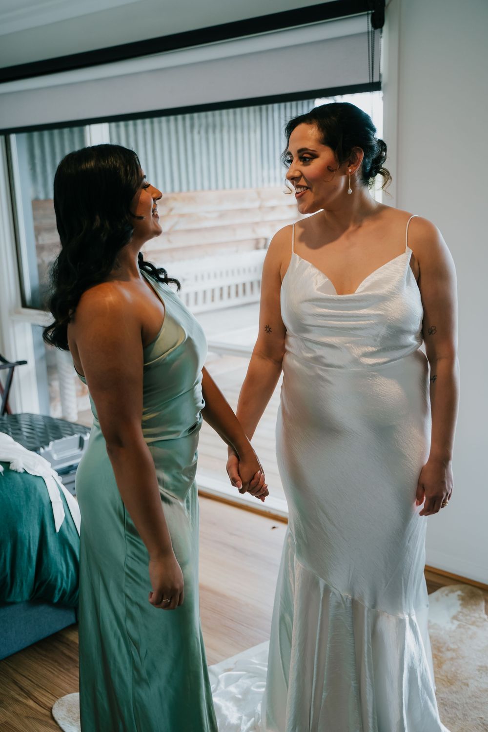 Two women in coordinating green bridesmaid dress and white wedding gown prepare for a special celebration.