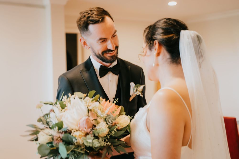 Elegant bride and groom share a loving moment during their wedding ceremony in a bright indoor venue.