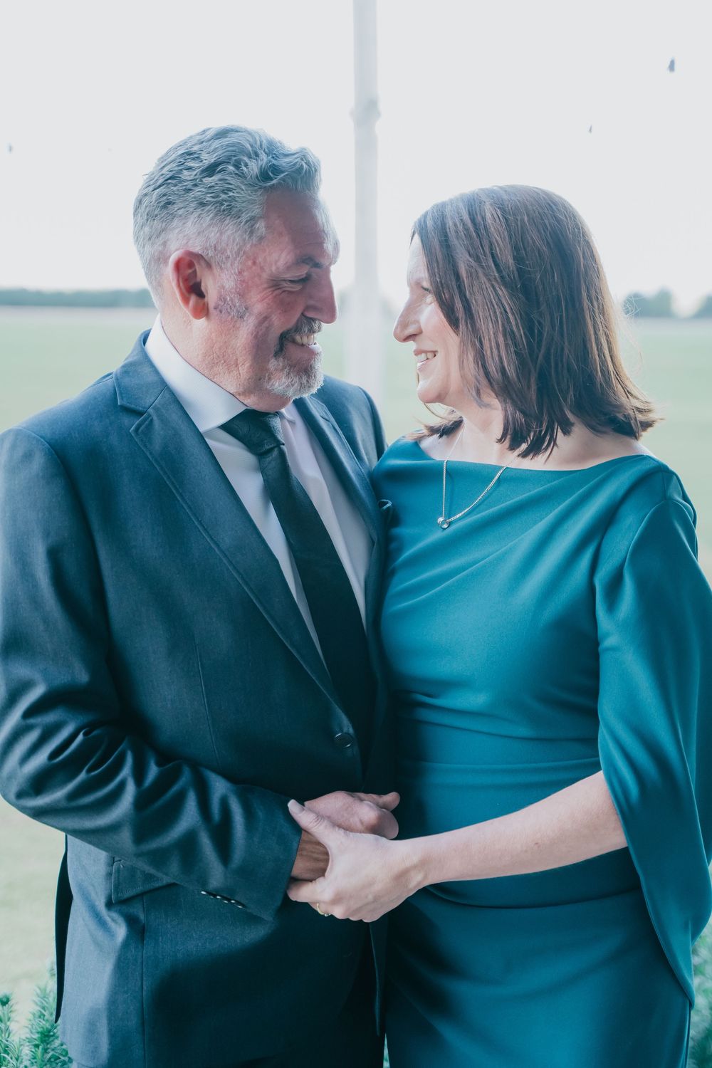Senior couple share a tender moment outdoors wearing formal attire, with the woman in teal and man in dark suit.