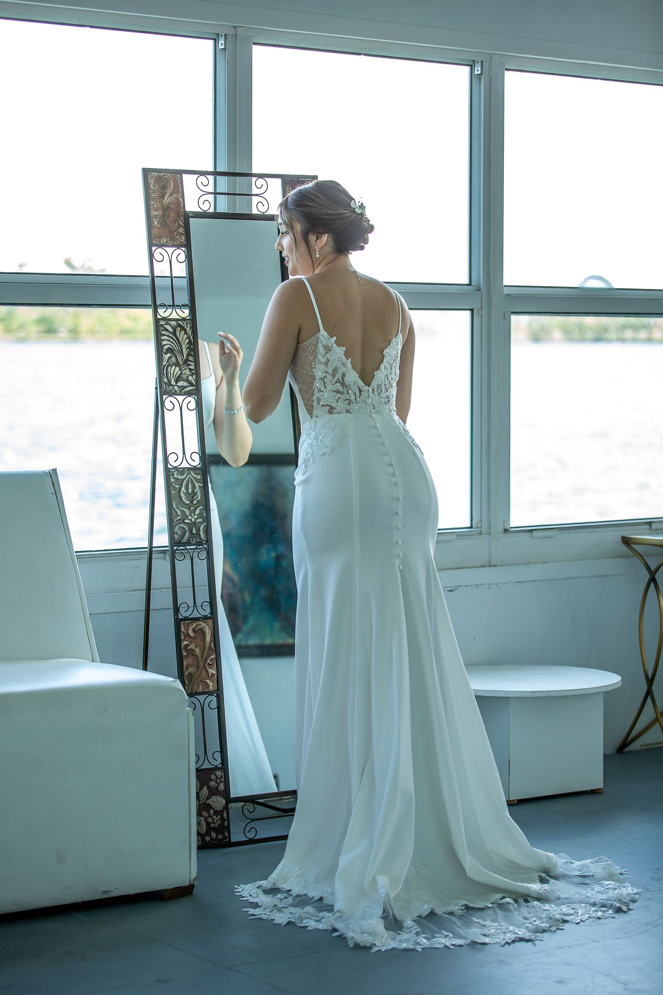 Five sequential shots showing back details of a flowing white wedding gown with lace overlay in a bright room.