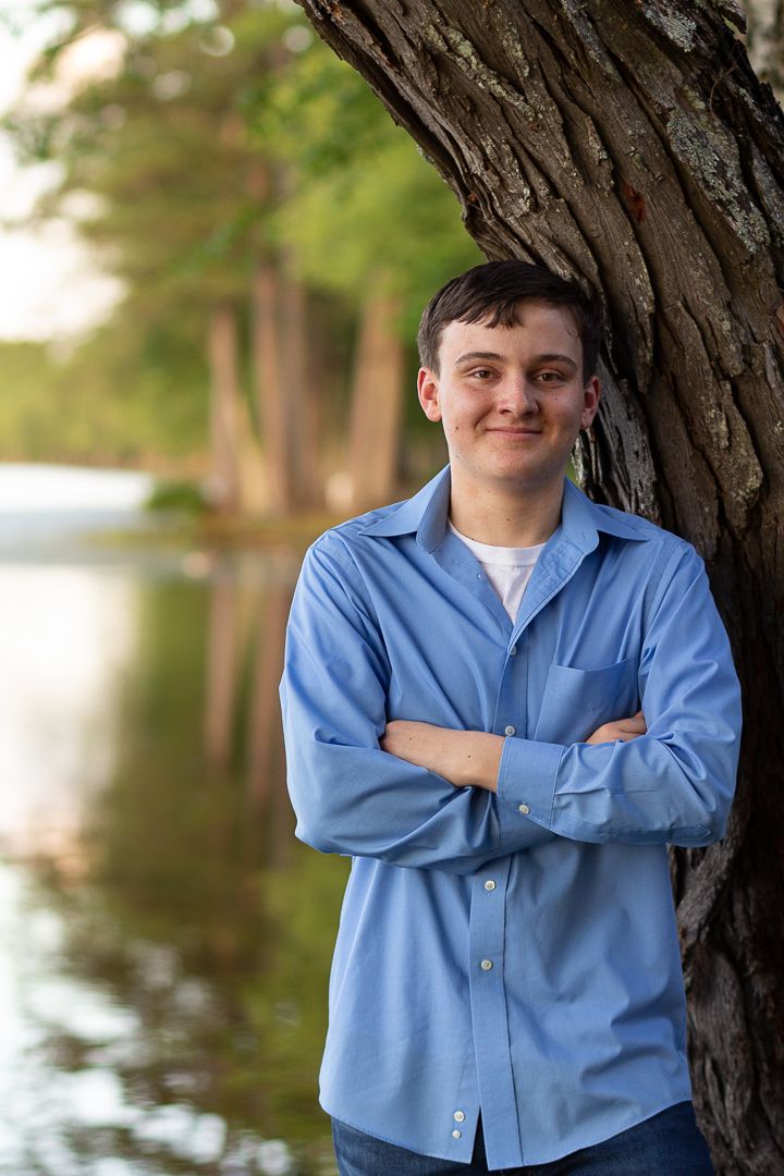 Portrait by a lake wearing a blue button-down shirt with crossed arms.