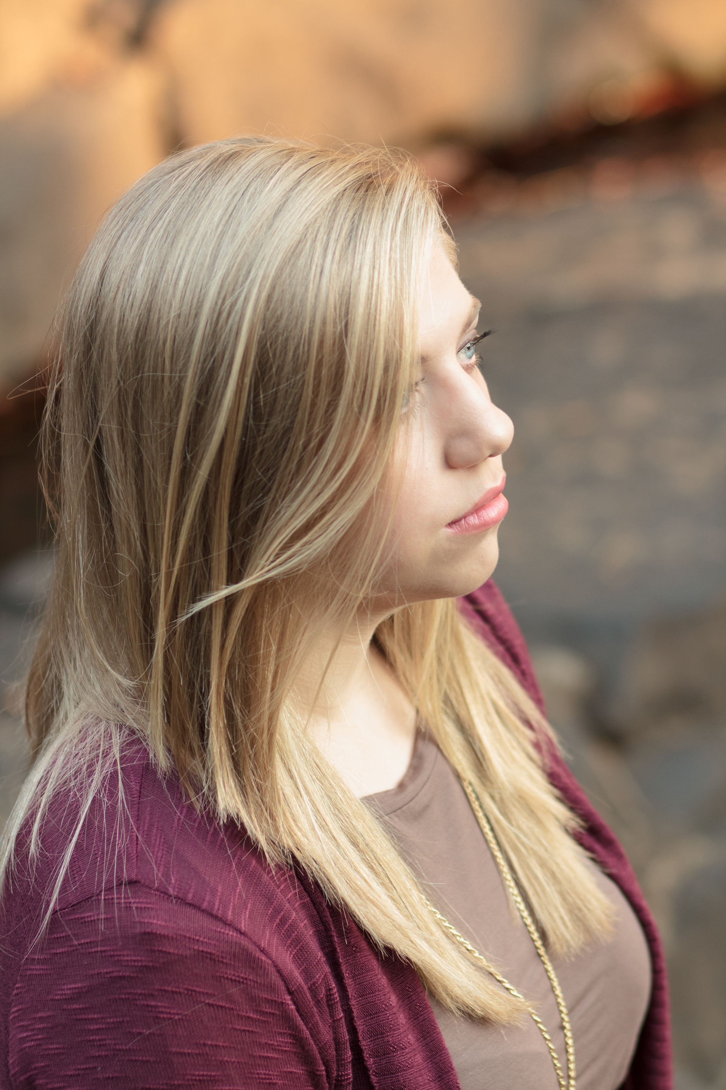 Profile view of someone with long blonde hair in a burgundy cardigan against a blurred background.