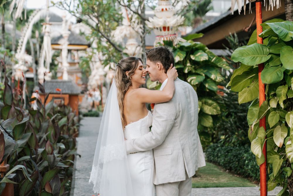 A romantic outdoor wedding scene at a tropical venue with foliage and architecture in the background.