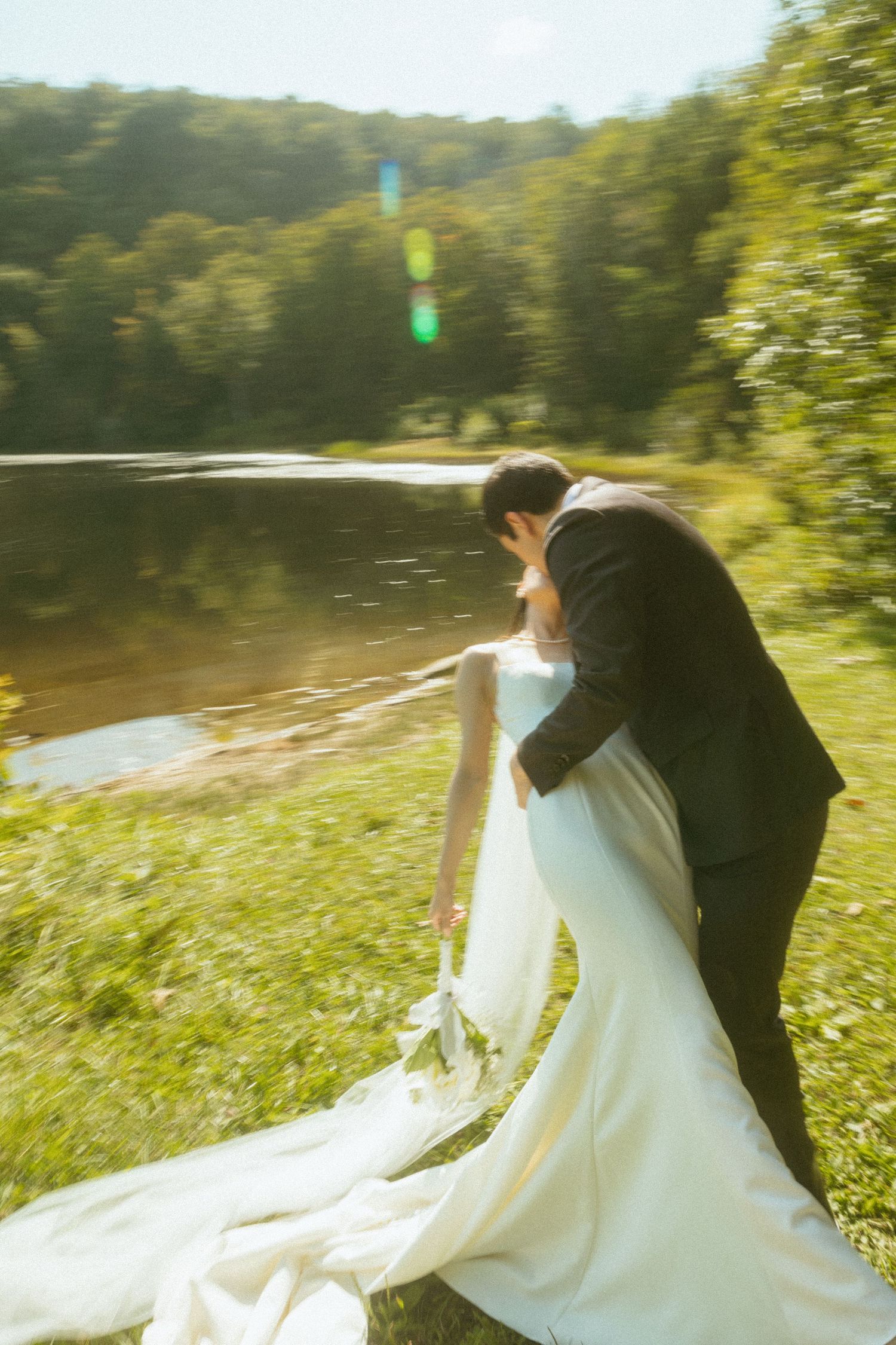 Wedding couple in formal attire photographed in a sunlit outdoor setting.