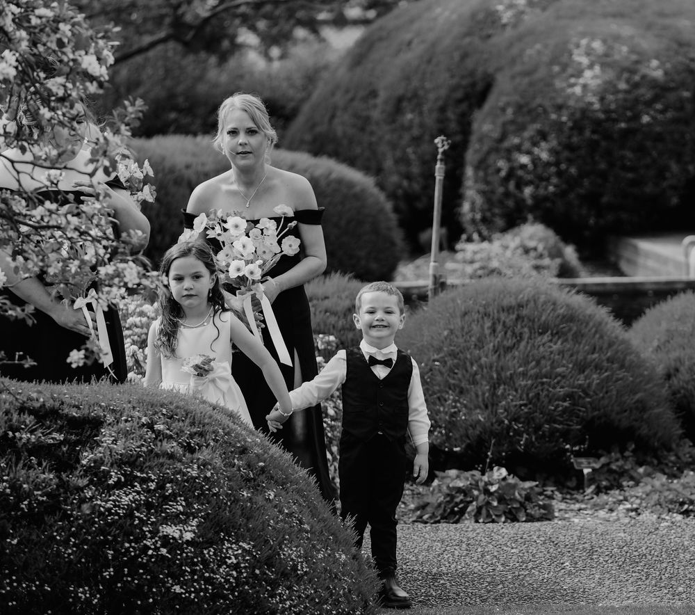 Children playing and running through garden pathways in formal attire.