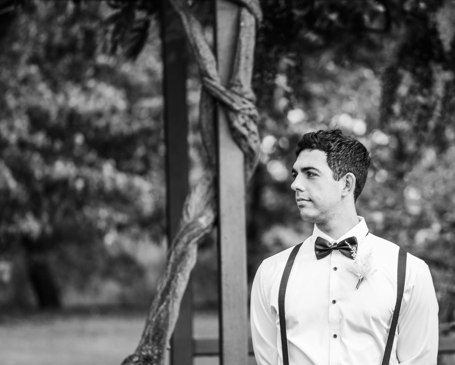 Wedding party members stand in formal attire against a natural outdoor background.