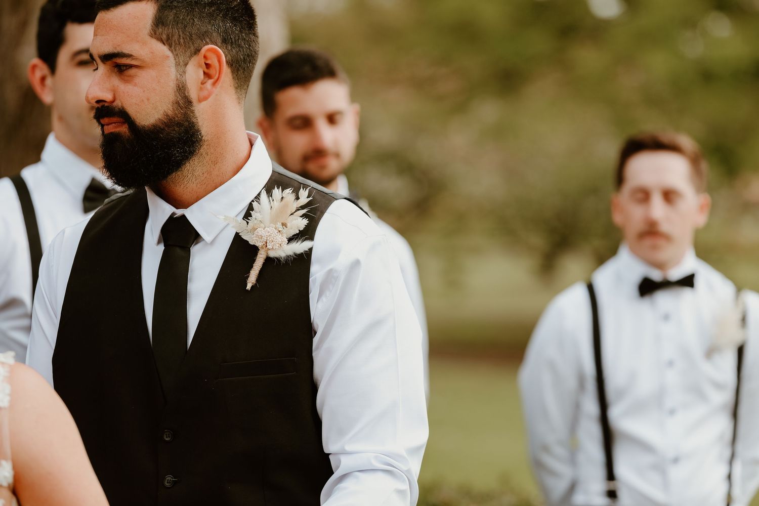 Wedding party members in formal attire stand together during an outdoor celebration.