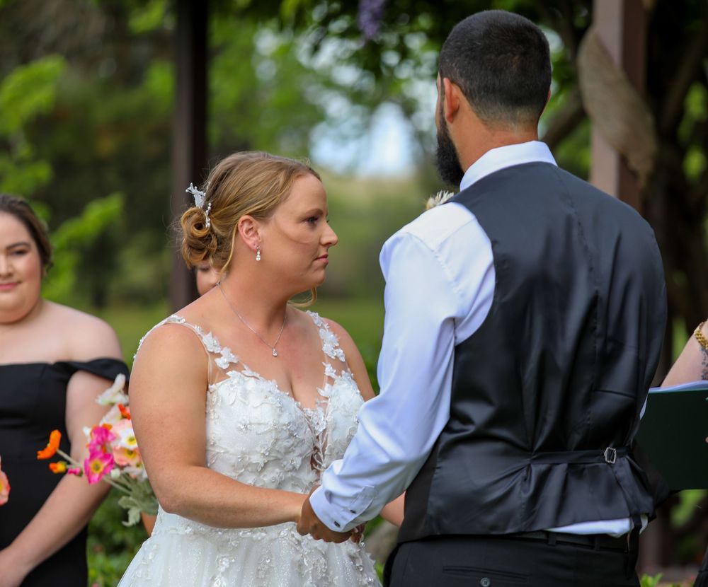 Wedding ceremony participants gathered outdoors with green foliage in the background.