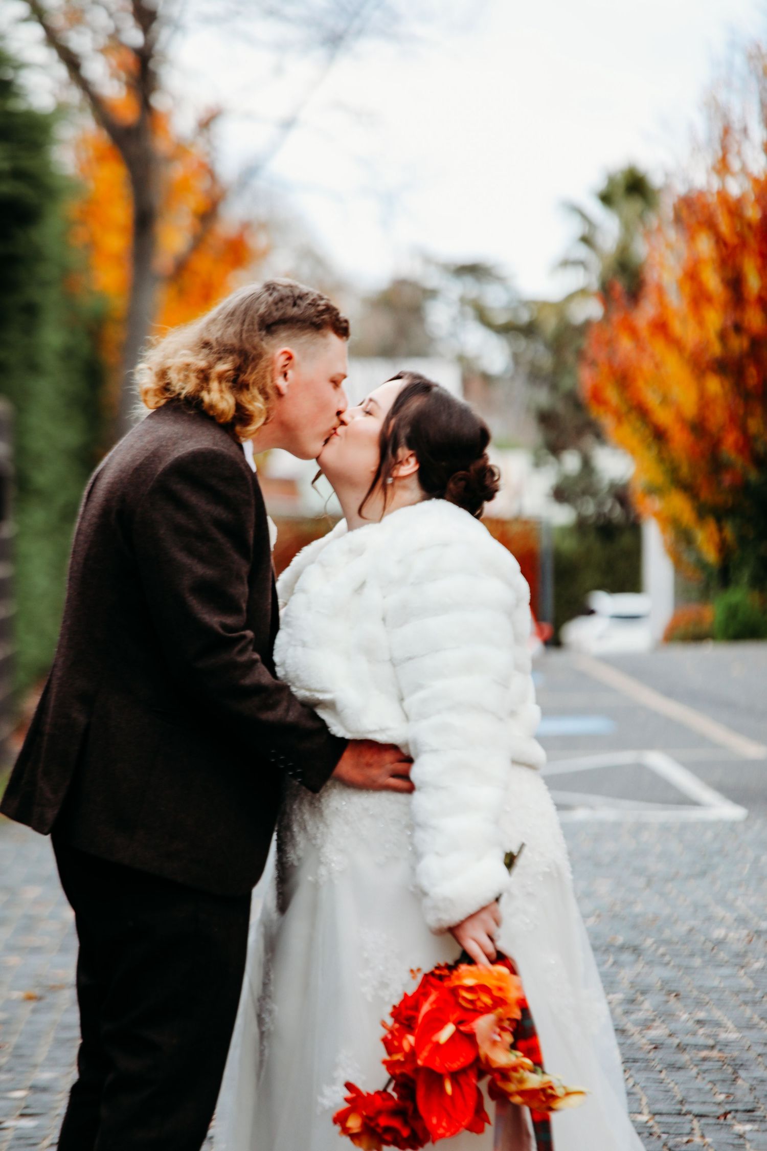 A romantic autumn wedding photo series showing a couple embracing on a leaf-covered street with orange foliage.