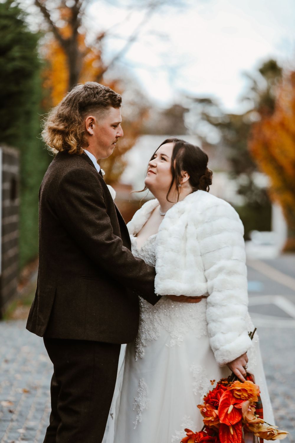 Wedding couple shares intimate moments outdoors with orange fall trees in the background.