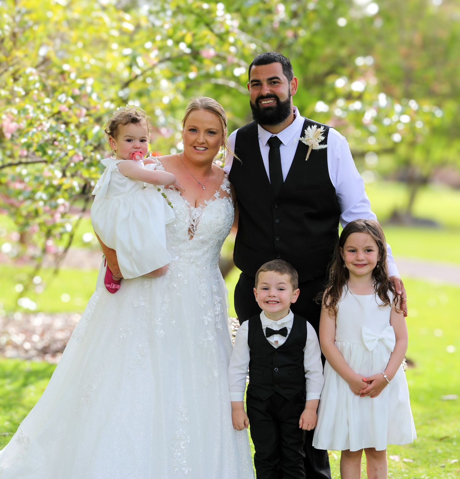 Wedding party poses together on a sunny day with blooming trees in the background.