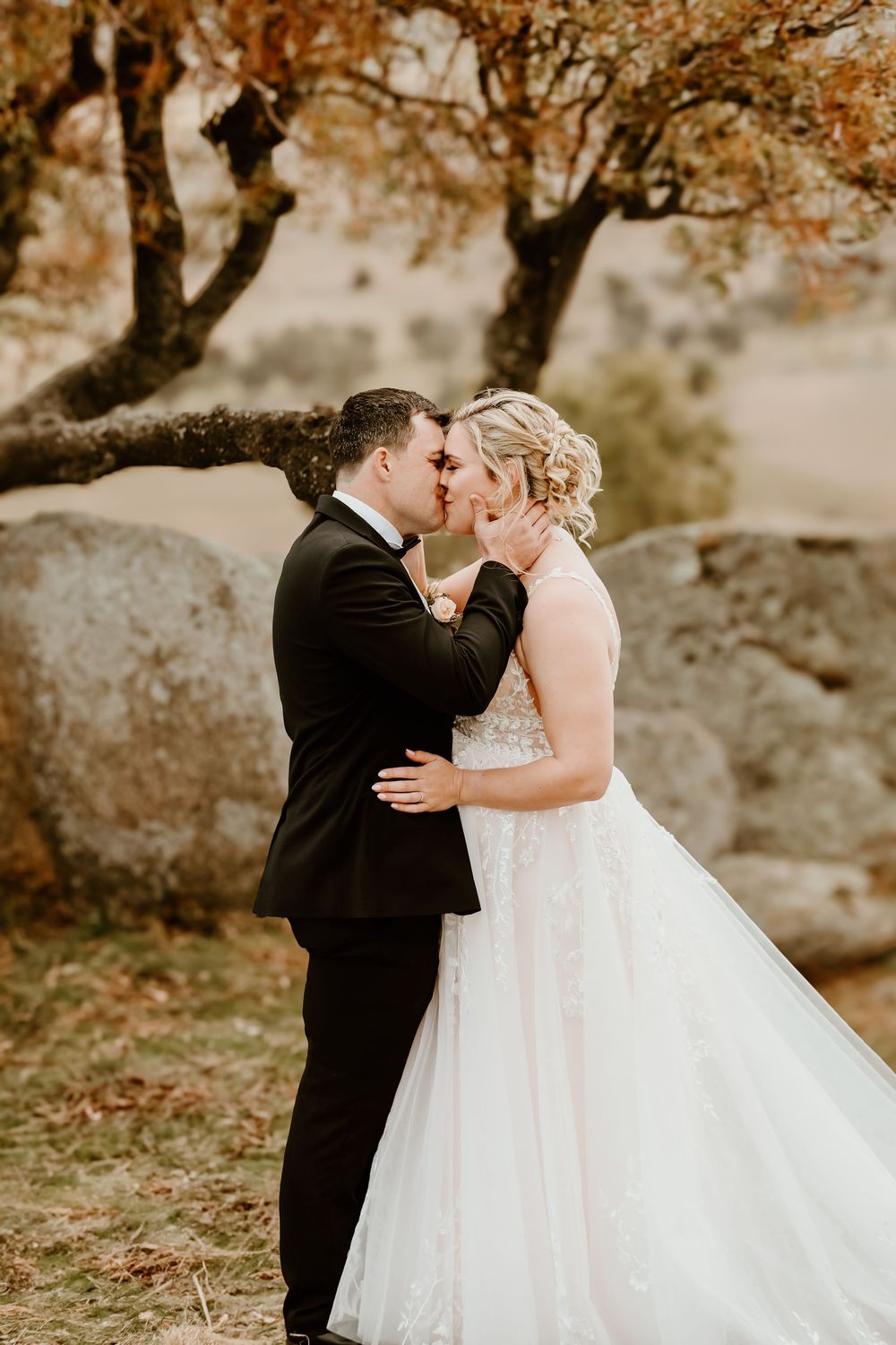 A romantic wedding moment captured under autumn trees in a natural setting.