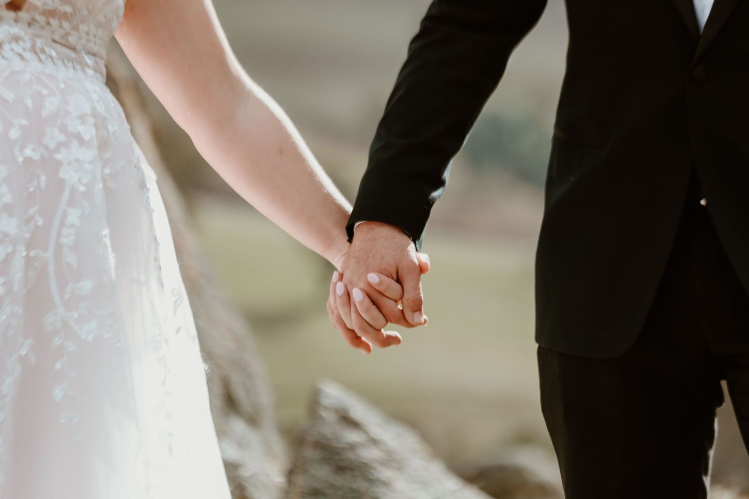 Close-up details of wedding couple holding hands during outdoor ceremony.