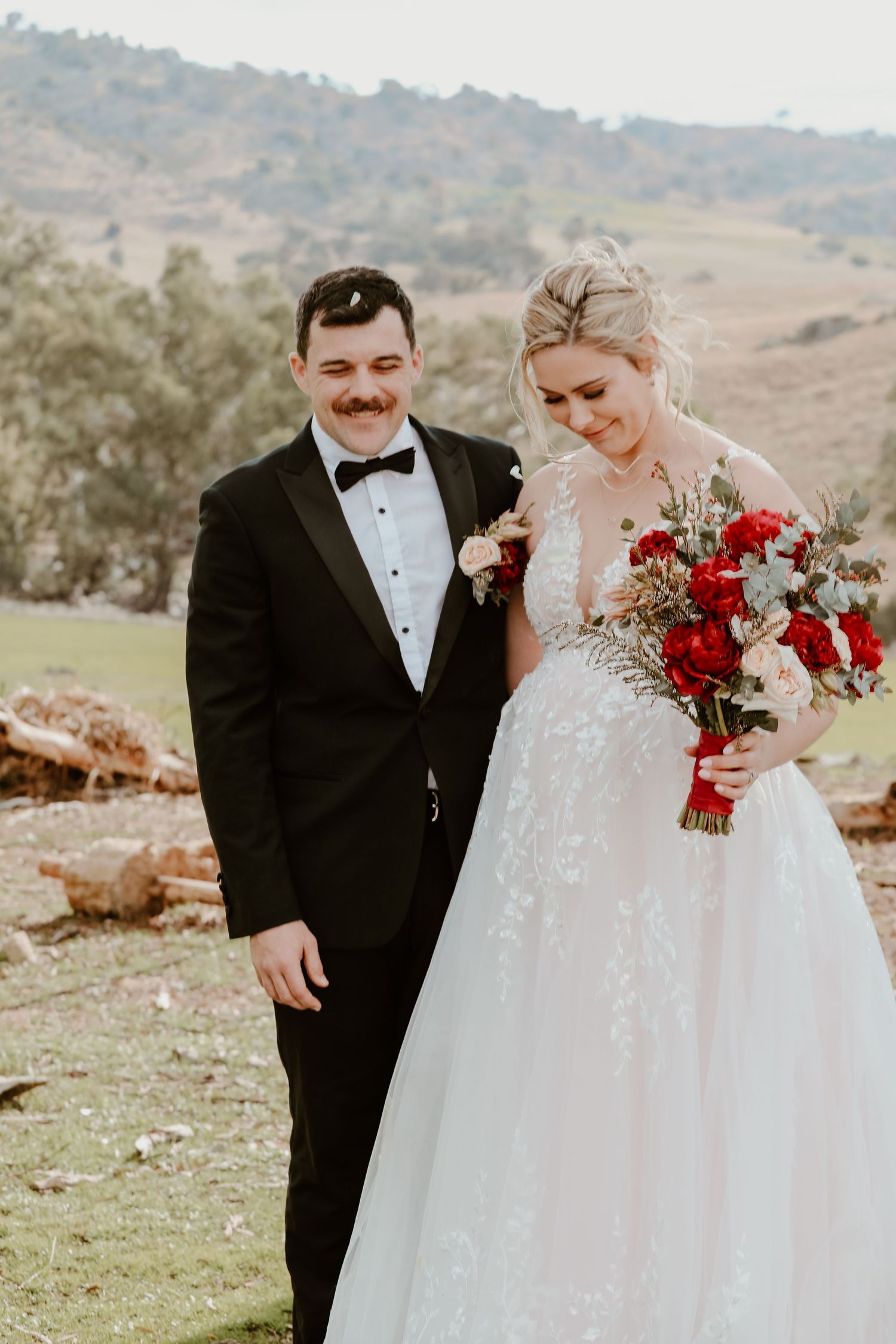 A couple in formal wedding attire share an intimate moment against a scenic mountain backdrop.