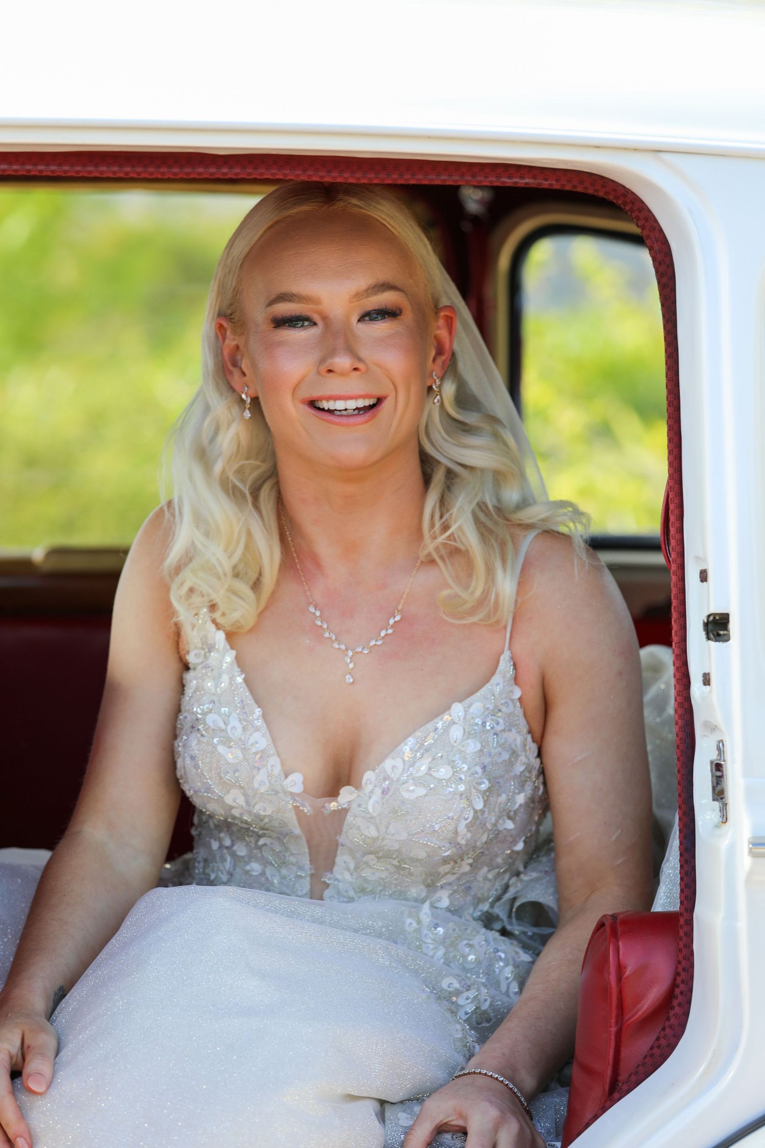 Bride sitting in vintage white car wearing sparkly wedding dress.