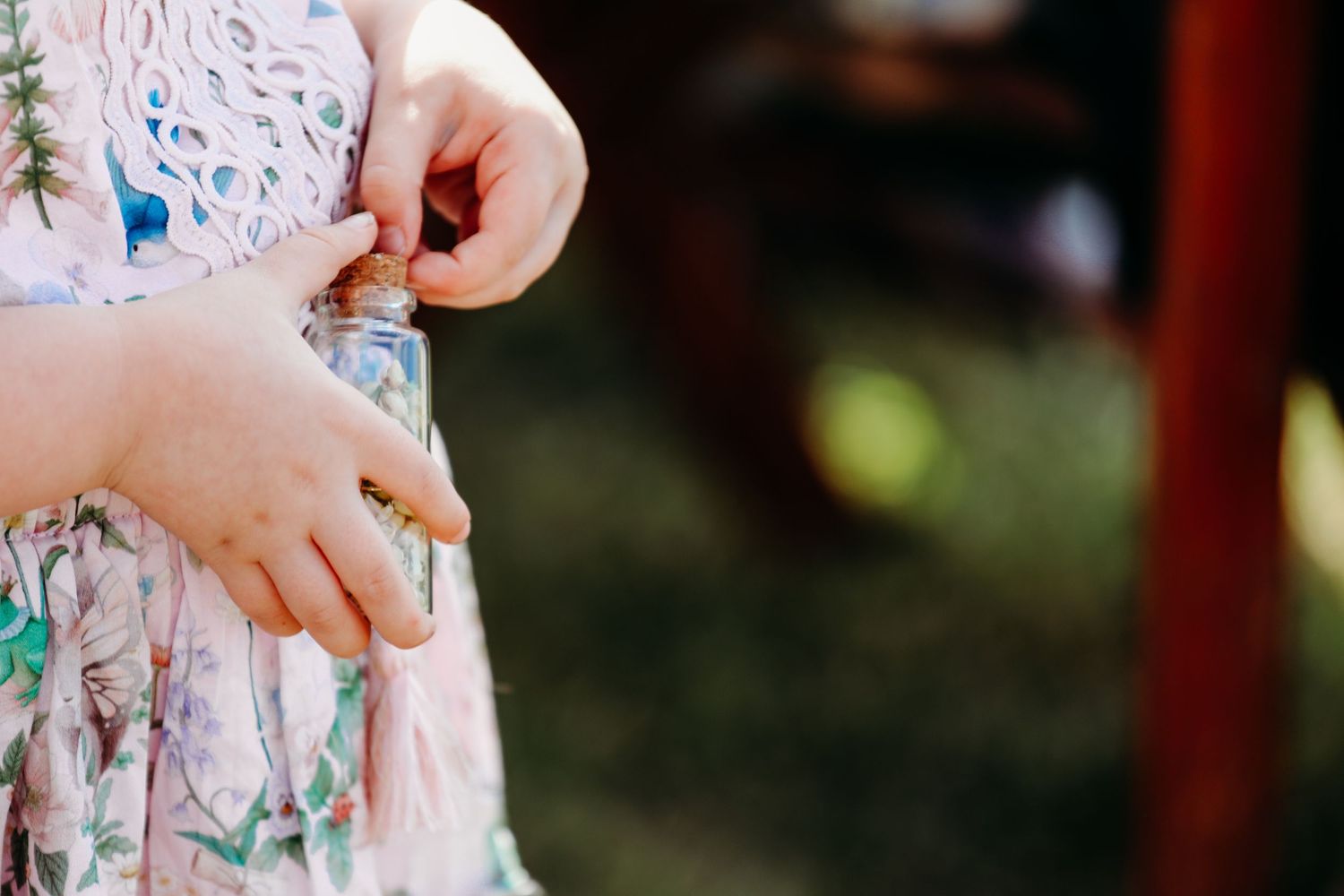 Close-up of small hands fidgeting with a colorful floral patterned dress in natural outdoor lighting.