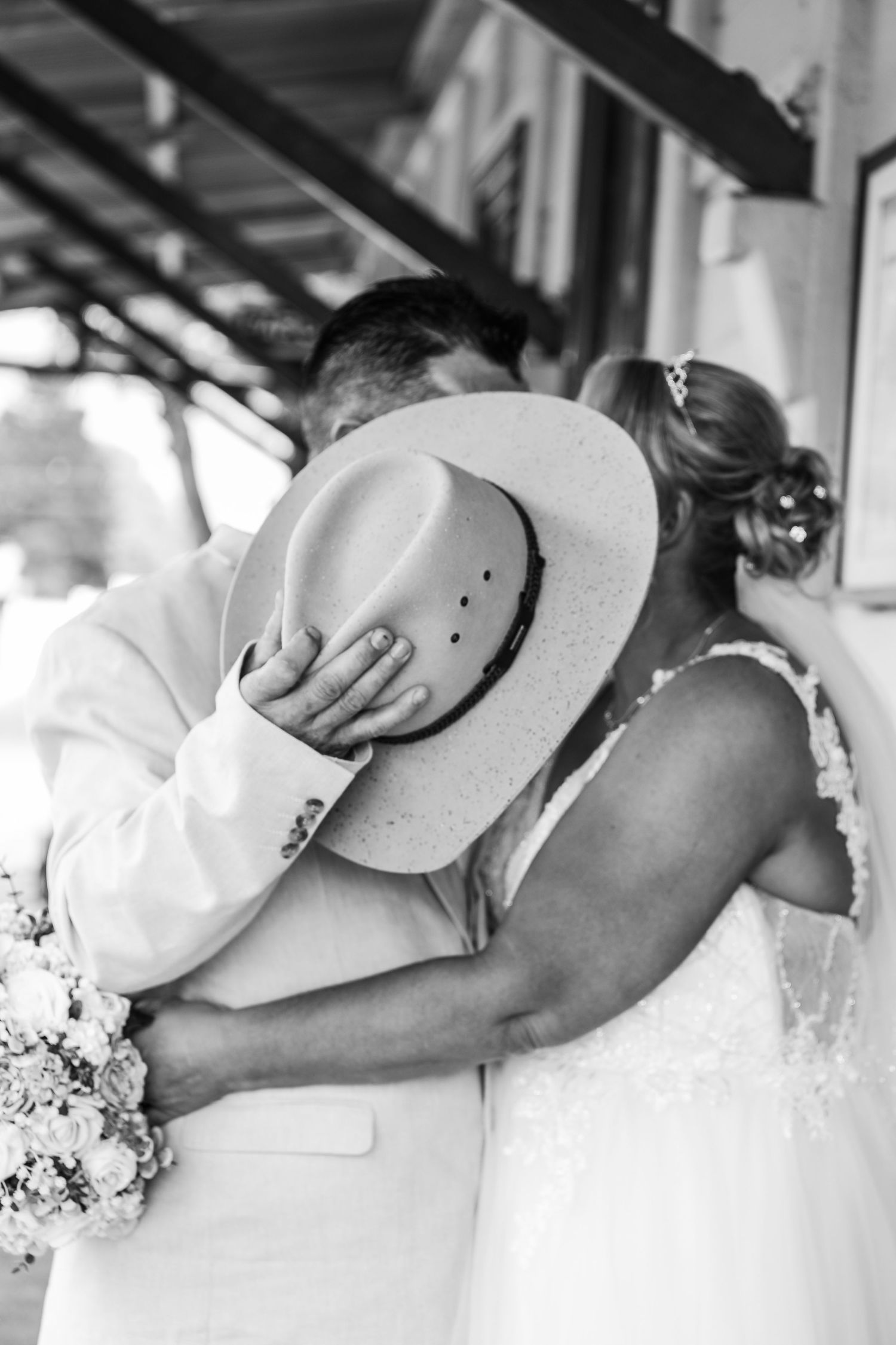 Romantic embrace between newlyweds with cowboy hat and white dress details.